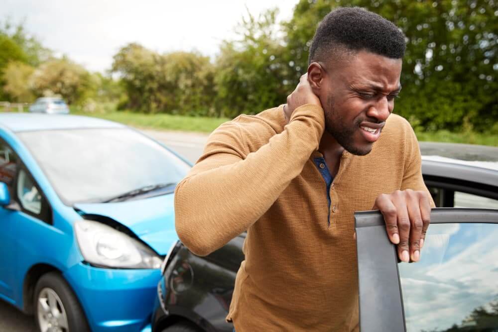 Man standing outside of car accident holding his neck.