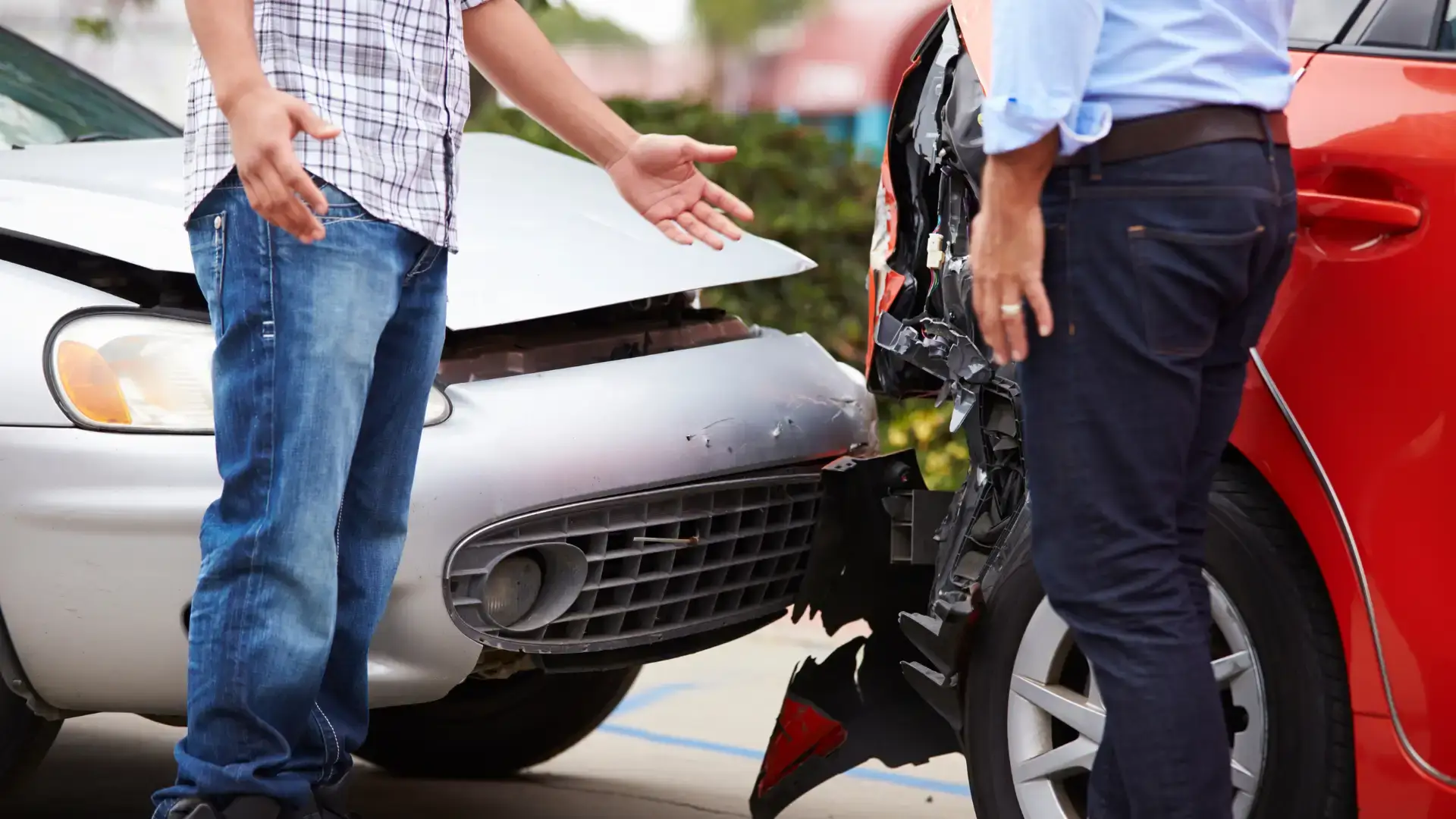 Two people discussing a car accident with visible front-end damage to both vehicles.