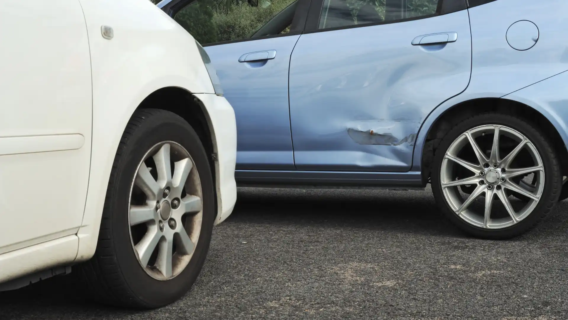 A side-impact collision showing a blue car with a dented door and a white car in the foreground.