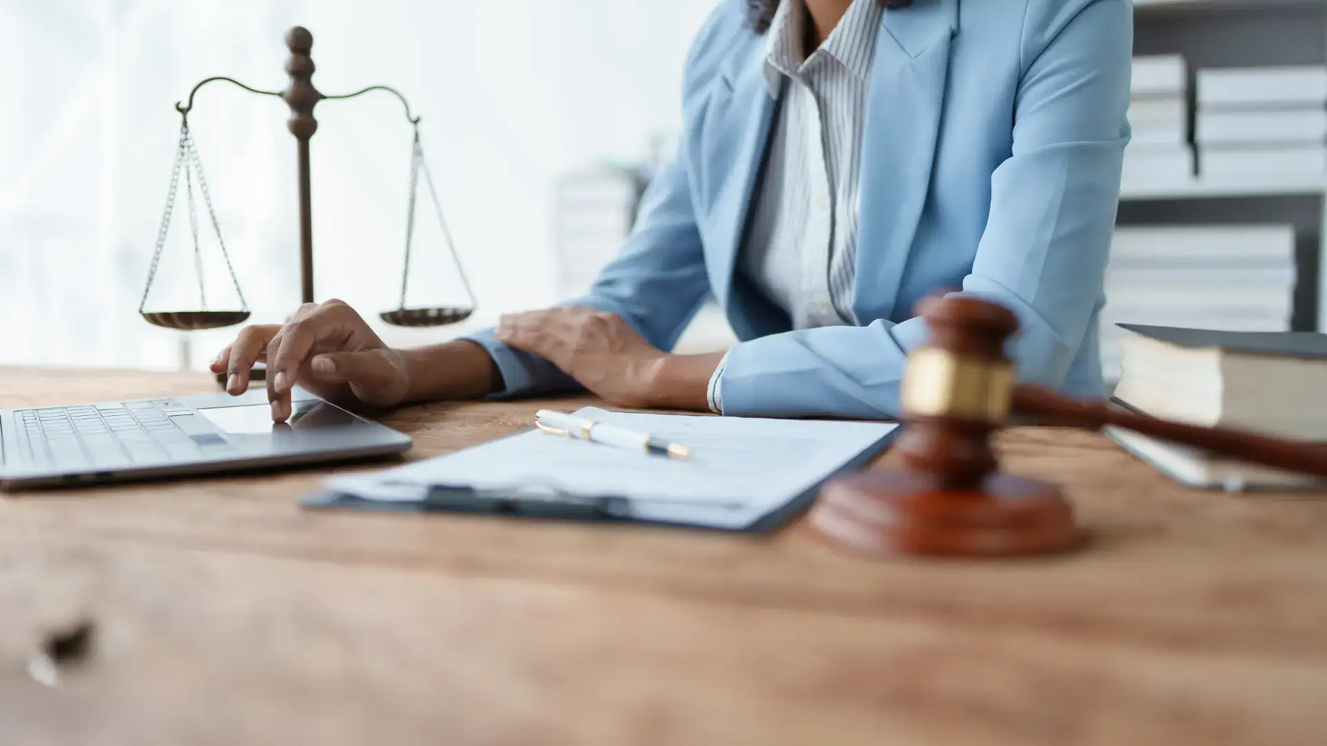 A lawyer in a blue suit working at a desk with legal documents, a gavel, and scales of justice.
