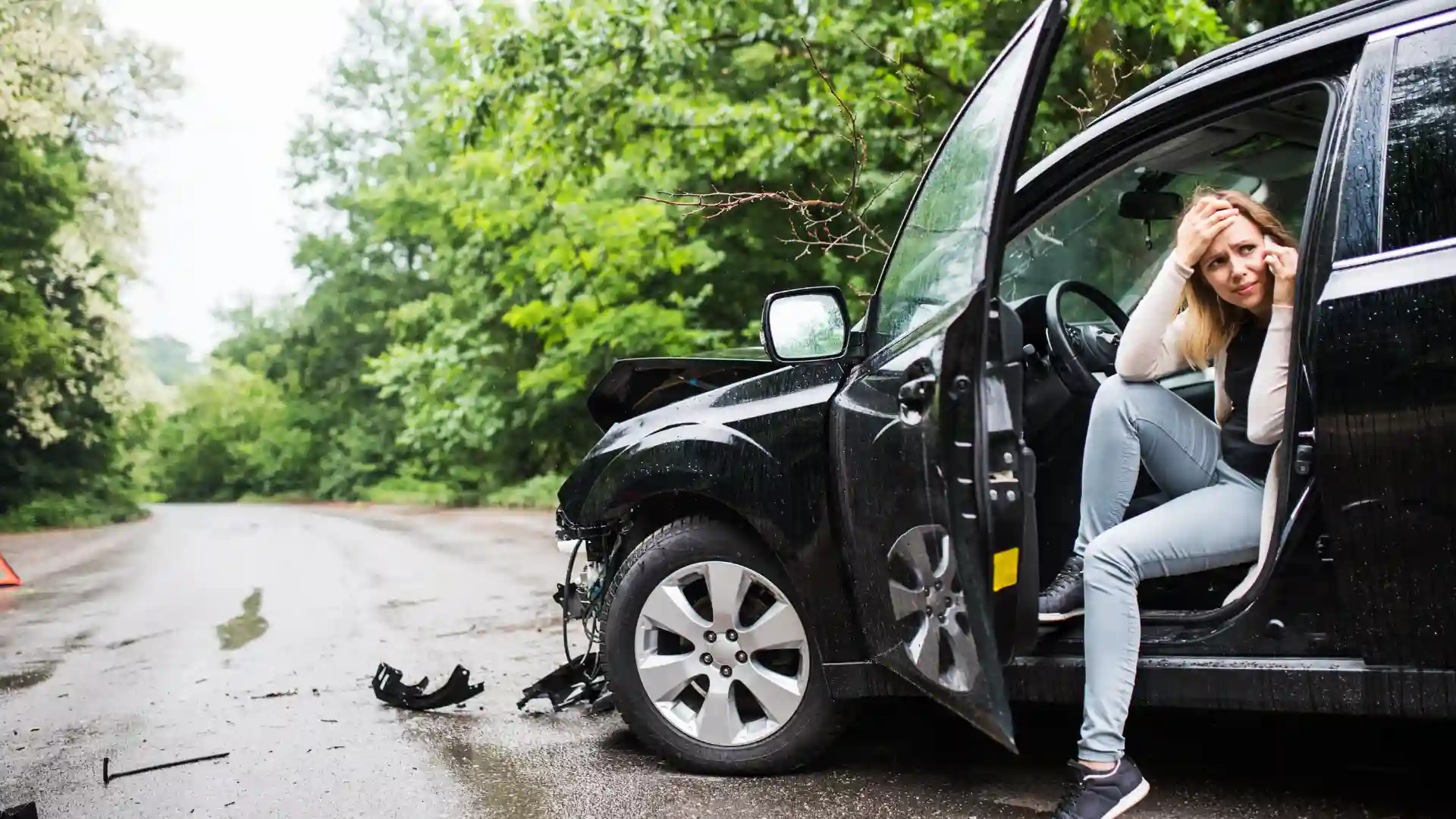 A damaged black car with an open door on a roadside.