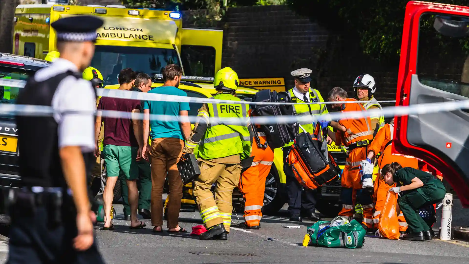 Emergency responders at the scene of an accident, with a fire truck and ambulance present, while onlookers observe."