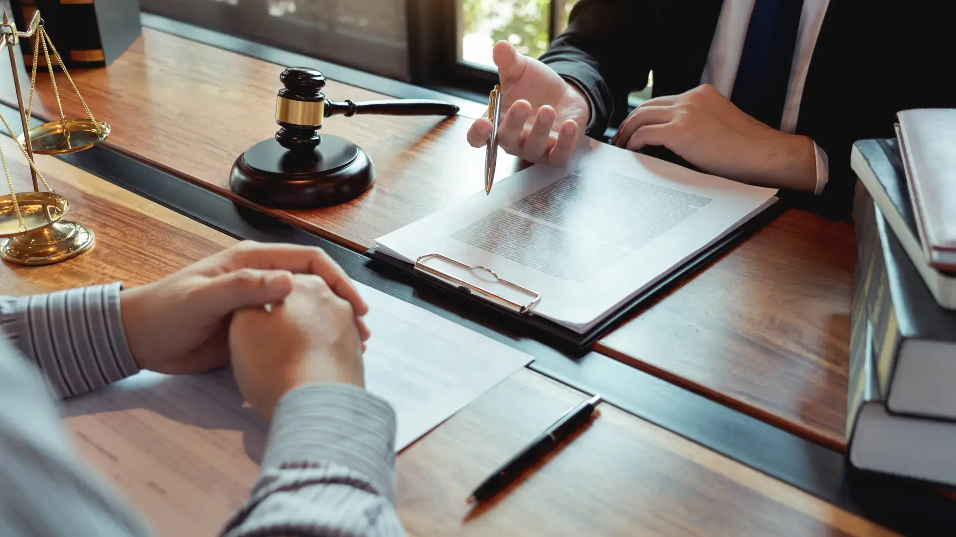 Two people shaking hands across a desk with legal documents, a gavel visible