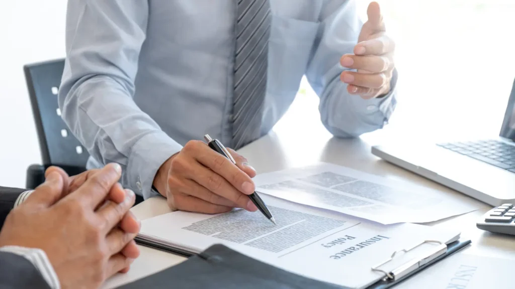 A close-up of a person signing a legal document, holding a pen with a formal hand gesture in a business meeting.