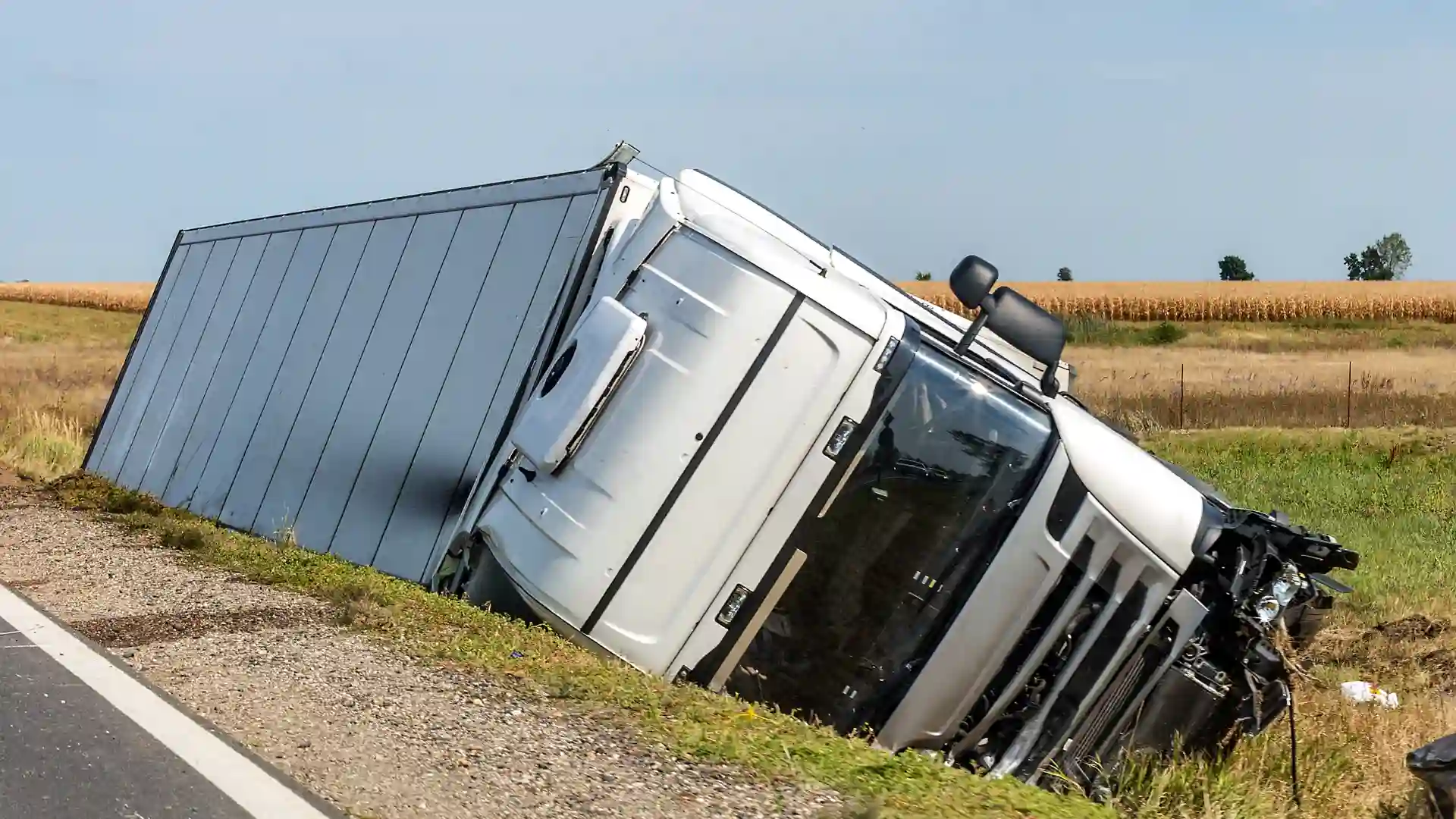 A truck on its side, partially in a ditch, with a recovery crew working in the background.