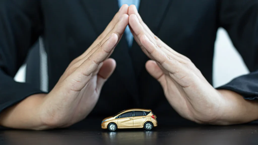 A person’s hands forming a protective shape around a small model car, symbolizing car insurance or protection.