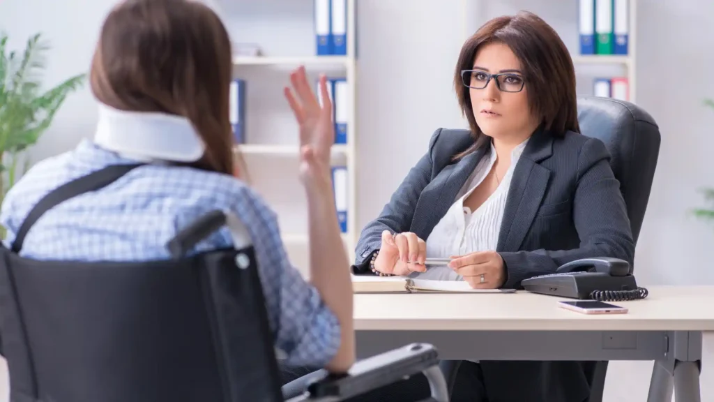 A woman in a wheelchair is talking with a lawyer during a consultation in an office setting, with the lawyer attentively listening and taking notes.