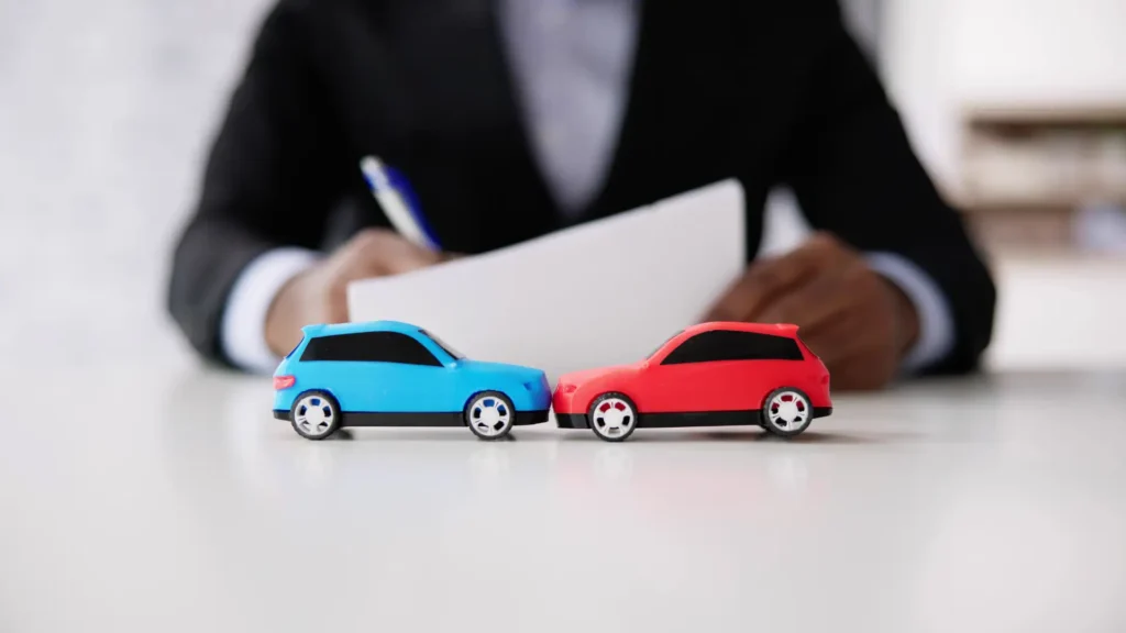 Toy cars representing a car accident with person writing in the background.