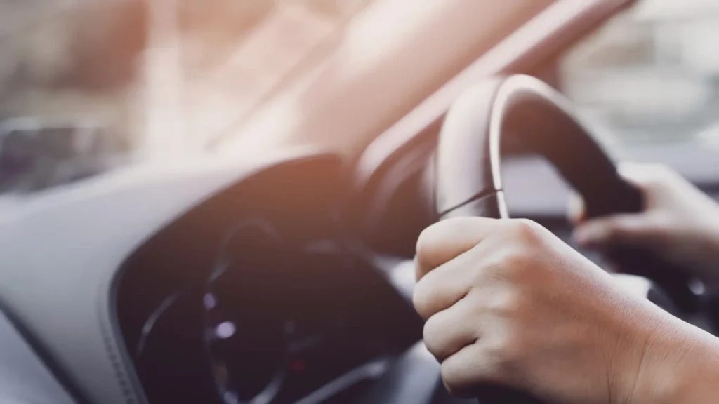 Close-up of a hand gripping a car steering wheel.